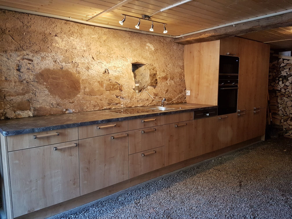 Eichenküche vor einer alten Bruchsteinwand unter Holzdecke